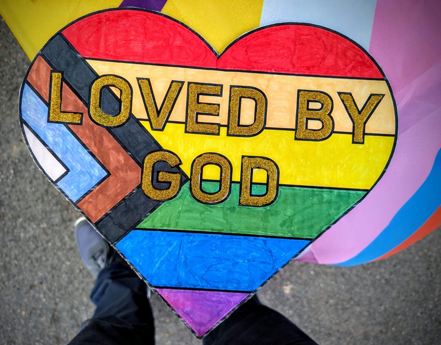 A Pride parade poster saying Loved by God with all appropriate colours in a heart shape